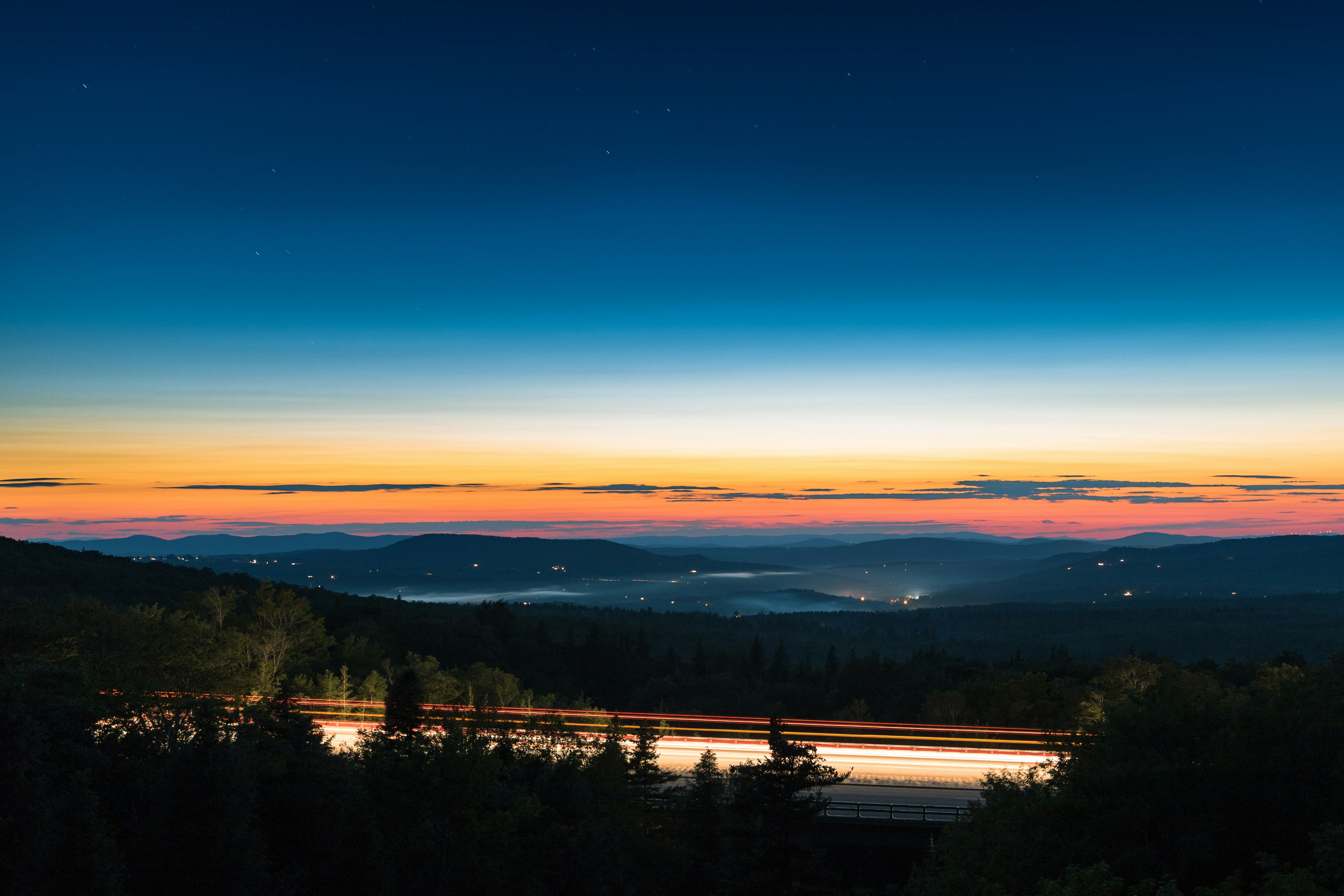 gray road surrounded by trees overseeing mountain rage during nighttie